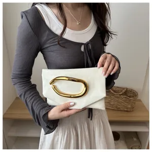 Detail view of a stylish white clutch bag featuring a bold abstract gold metal handle, held by model.