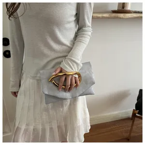 Detail view of a grey clutch bag featuring a striking golden metal handle, lifestyle setting.