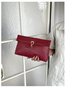 Close-up detail van een rode gewoven envelop clutch tas met elegante metalen gesp in hand.