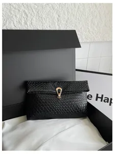 Detail zwarte geweven envelop clutch tas, minimalistisch ontwerp met elegante metalen gesp.