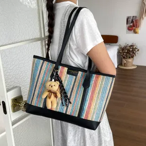 Detailed view of the colorful striped straw tote bag featuring black leather trim and cute bear charm.