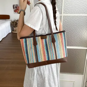 Detailed view of a stylish color-block striped straw beach tote bag with brown leather trim.