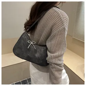 Detailed shot of textured grey underarm handbag with sparkling rhinestone bow pendant charm.
