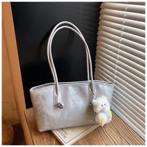 Close-up of a silver PU leather shoulder tote bag with double handles and a cute plush charm.