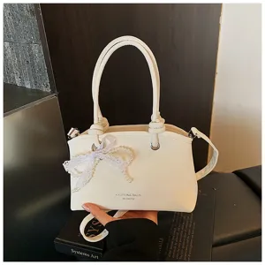 Detailaufnahme der weißen Modetasche mit einem zarten Perlen-Spitzen-Schleifen-Anhänger.
