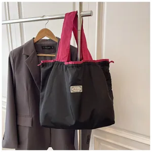 Zwarte opvouwbare shopper tas met roze contrastriemen en een handige trekkoordsluiting.