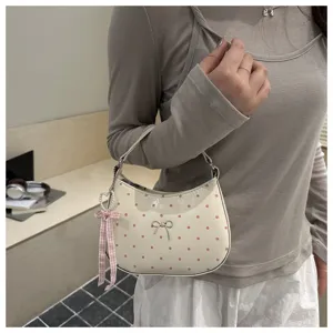 Bolso bandolera de hombro luna con lunares dulces y detalle de lazo y colgante.