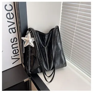 Detail view of black patent leather tote bag, glossy finish and star charm detail.