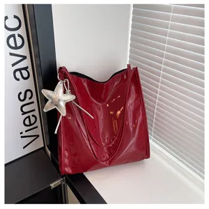 Red patent leather tote bag detail with shiny silver star pendant charm hanging on side.