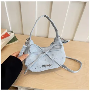 Close-up detail of light blue bow shoulder bag with star pattern and metal logo tag.