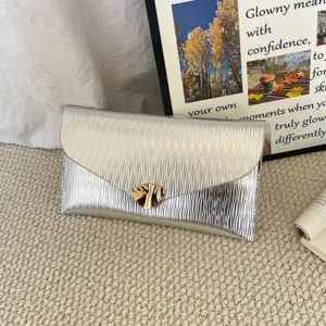 Close-up detail of silver metallic envelope clutch bag with golden irregular clasp closure.