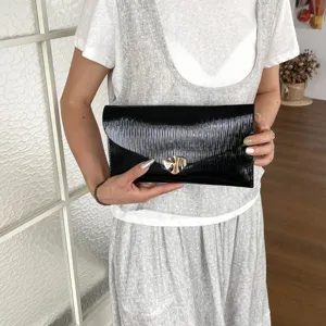 Detailed view of the black pleated envelope clutch bag featuring a sleek metallic gold clasp.