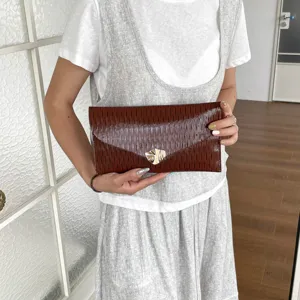 Detail shot of a brown textured envelope clutch bag held in hand, showing unique metal clasp.