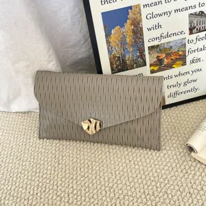 Close-up of gray textured envelope clutch bag with golden abstract metal clasp detail.