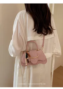 Vista detallada de un bolso rosa con diseño ondulado, detalle metálico y colgante de cuentas.