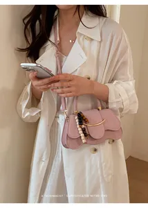 Primer plano del elegante bolso rosa con solapa ondulada, barra metálica y detalles de perlas.