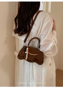 Vista detallada del bolso marrón con solapa ondulada y abalorio de cuentas, diseño elegante.