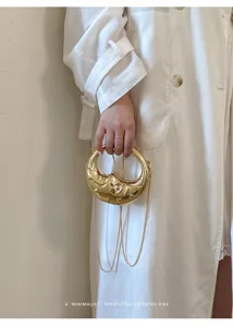 Detailaufnahme einer luxuriösen goldenen Mondsichel Handtasche aus Metall mit Kette.