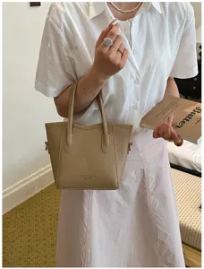 Beige leather bucket bag detail, elegant casual handbag with dual top handles and rings.