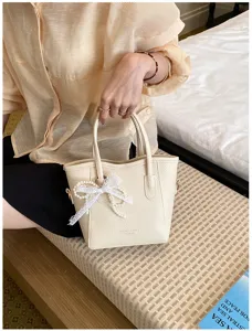 Close-up detail of the elegant beige bucket handbag featuring delicate pearl lace bow pendant.