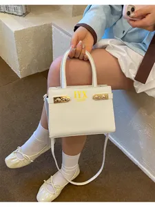 Detailed view of white fashion commuter handbag with golden letters and hardware decor.