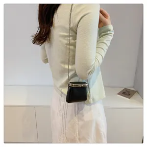 Detail of mini black kiss-lock crossbody bag with metal chain strap worn by model.