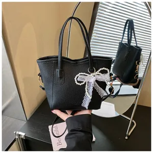 Black leather bucket bag detail showing exquisite pearl lace bow pendant and texture.