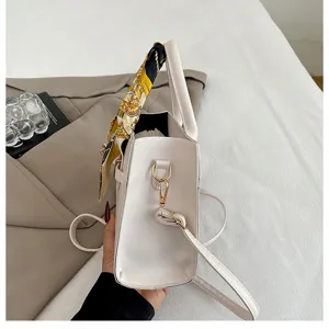 Detail view of a white women handbag with elegant printed scarf and metal hardware.