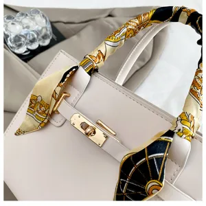Close-up of elegant off-white women handbag with chic printed scarf wrapped handle and gold lock.