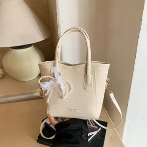 Beige faux leather bucket bag with pearl lace bow pendant, stylish daily commuter tote handbag.