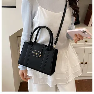 Gros plan sur le sac à main en cuir noir porté par le mannequin avec plaque métallique.