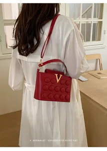 Vista dettagliata della borsa a tracolla in pelle rossa con logo V dorato e trapuntatura.