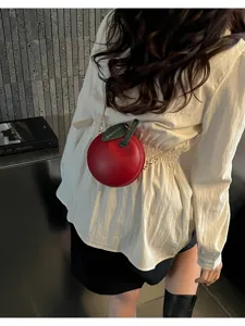 Detail view of stylish red apple shaped mini crossbody bag with chic chain strap and leaf detail.
