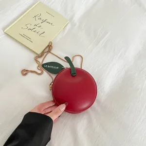 Close-up of a stylish red apple-shaped mini crossbody bag with a green chain and leaf.