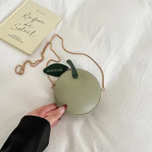 Close-up detail of green apple-shaped round crossbody bag with gold chain and leaf tag.