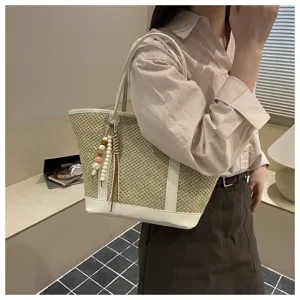 Detail view of woven straw tote bag with white leather trim and charming wooden bead charms.