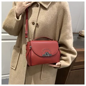 Détail de sac à épaule en cuir rouge avec fermoir métallique élégant et rivets sur le rabat.