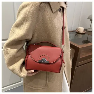 Vue détaillée du sac bandoulière élégant en cuir rouge avec serrure métallique et rivets.