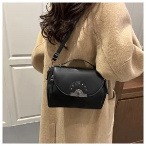 Détail du sac à épaule en cuir noir avec rabat, serrure en métal et bandoulière élégante.