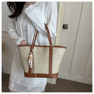 Close-up detail of stylish straw woven tote bag with brown leather trim and cute beaded charm.