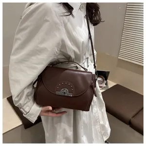Gros plan élégant d'un sac à bandoulière marron foncé pour femme avec serrure métallique.