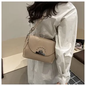 Sac bandoulière tendance en cuir beige avec fermoir métallique et clous élégants.