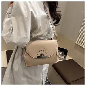 Sac à épaule élégant beige avec fermeture métallique et clous, idéal pour un look quotidien.