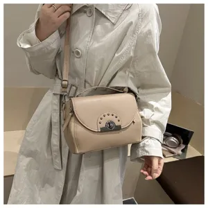 Élégant sac bandoulière beige avec fermoir tourniquet en métal et détails de rivets.