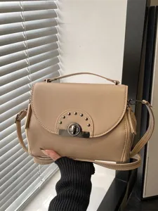 Sac à bandoulière beige élégant pour femme avec serrure métallique et rivets chics.