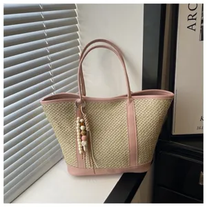 Detailed view of women straw woven tote bag with pink leather trim and chic bead charm for summer.