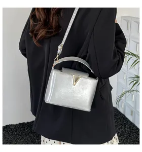 Sac à bandoulière seau argenté métallique élégant pour femmes avec fermoir V doré stylé.