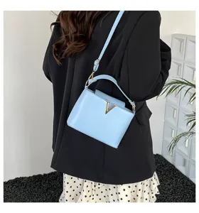 Détail de sac seau bandoulière en cuir bleu clair, avec logo V métallique et sangle élégante.