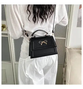 Vue détaillée d'un petit sac bandoulière noir pour femme avec un élégant nœud doré chic.