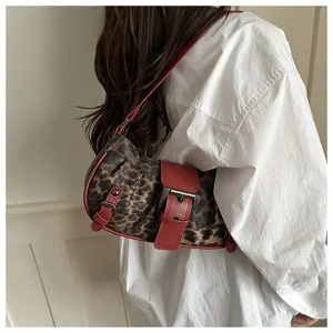 Detalle de bolso de hombro medialuna con estampado de leopardo y hebillas rojas.